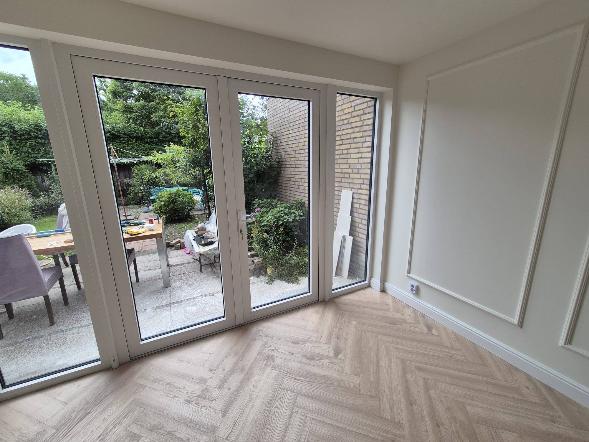 Home extension interior with herringbone floor and garden view in Waalre